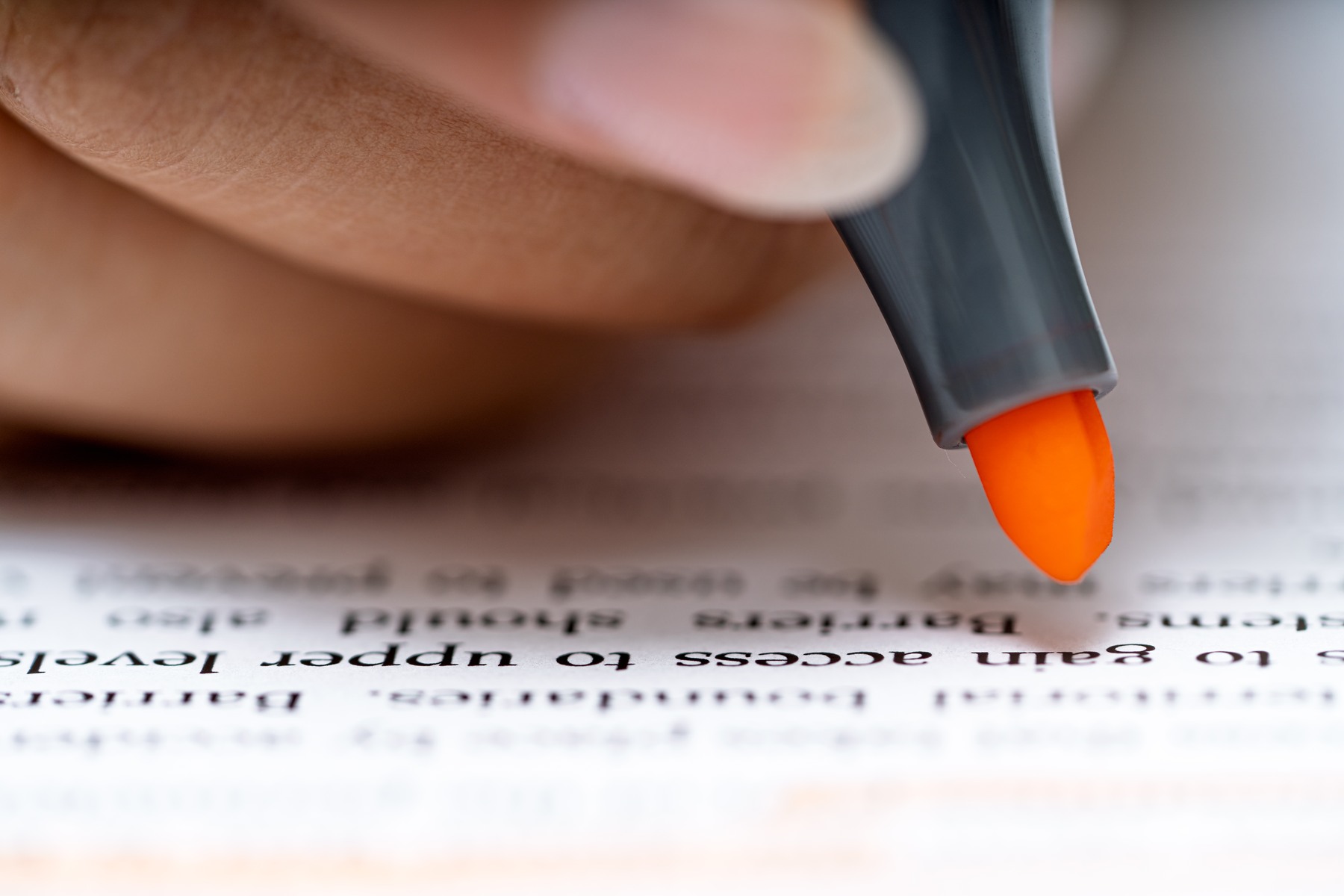 A hand holds an orange highlighter above printed text.
