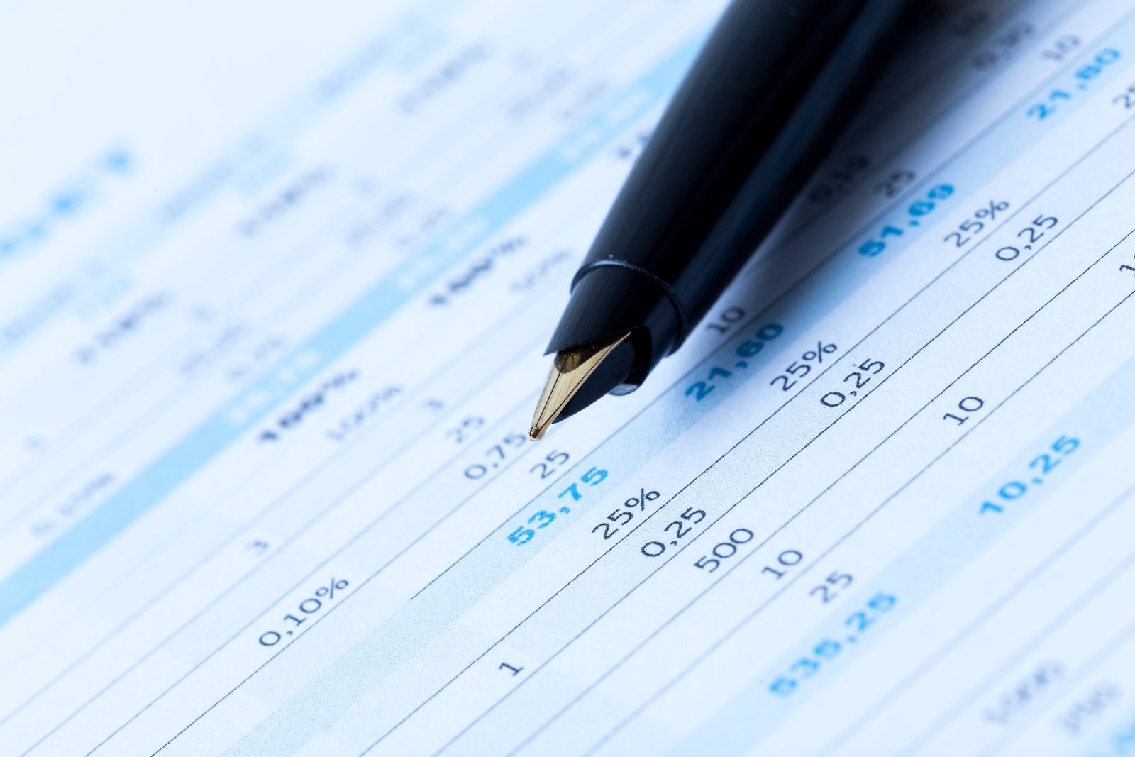 Close view of a fountain pen tip resting on a printed financial table filled with columns of figures and percentages